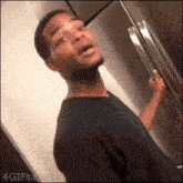 a man in a black shirt is standing in front of a refrigerator with his mouth open