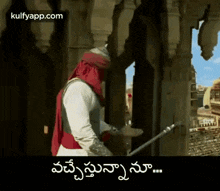 a man in a turban is standing in front of a building with a sword in his hand .