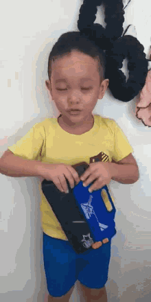 a young boy wearing a yellow shirt and blue shorts is holding a blue and black item .
