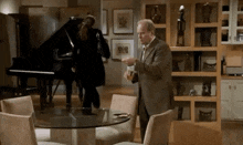 a man in a suit and tie is standing in a dining room next to a piano .