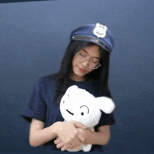 a woman wearing a police hat and glasses is holding a stuffed animal .