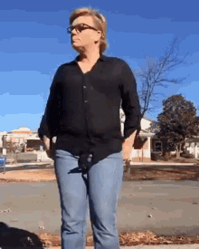 a woman wearing glasses and a black shirt is standing on a sidewalk .