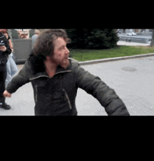 a man in a black jacket is walking down a sidewalk with his arms outstretched