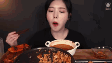 a woman is eating food with chopsticks from a pan while another person looks on .