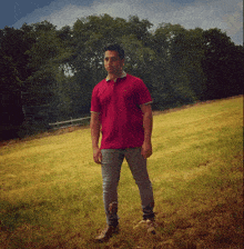 a man in a red shirt with a lacoste logo on it stands in a field