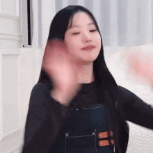 a woman with long black hair is waving at the camera .