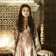 a woman in a long dress is standing in front of a fireplace with a pattern on it