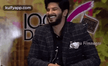 a man in a suit is laughing and smiling while standing in front of a wall .