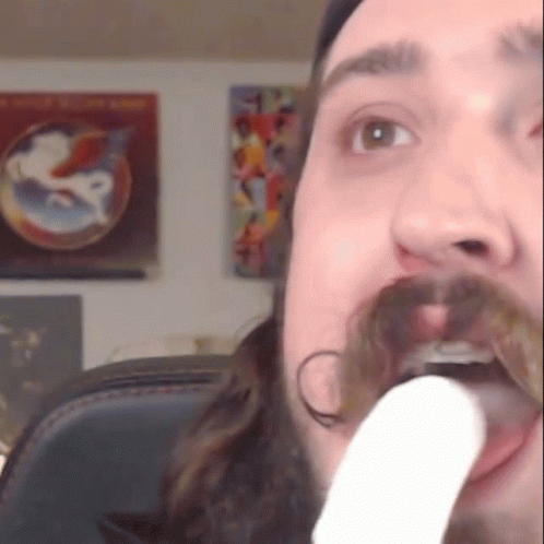 a man with a beard and mustache holds a white object in his mouth