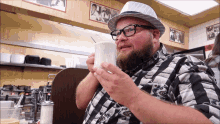 a man wearing glasses and a hat is drinking from a cup