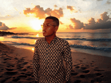 a man standing on a beach smoking a cigarette at sunset