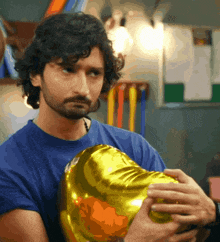 a man in a blue shirt is holding a gold balloon in his hands