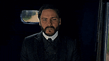 a man with a beard wearing a suit and tie is looking out a window