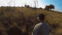 a man stands in a field of tall grass with trees in the background