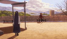 a man sits on a bench while a woman stands in front of a stone wall