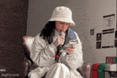 a woman wearing a white hat is sitting in a chair holding a microphone and looking at her phone .