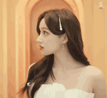a woman in a white dress with pearls in her hair looks at the camera