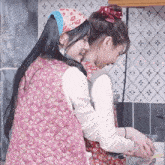 a woman in a pink floral vest is hugging another woman in an apron