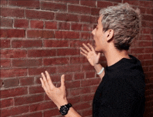 a man wearing a black shirt and a black watch is standing in front of a brick wall