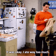 a man is standing in a kitchen holding a jacket and saying `` it was okay , i ate way too much ''