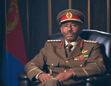 a man in a military uniform is sitting in a chair in front of a flag