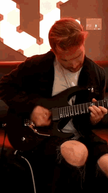 a man in a black jacket is playing a guitar with the letter t on the neck