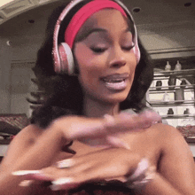 a woman wearing headphones and a pink headband looks at her nails