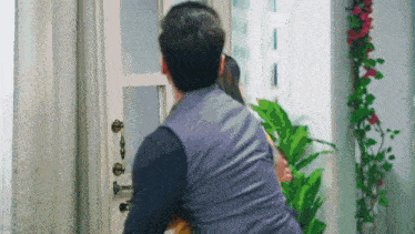 a man and woman are standing in front of a door with a plant in the background .