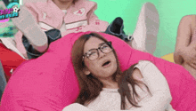 a woman wearing glasses laying on a pink bean bag