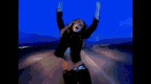 a woman is dancing on a road with her arms outstretched in front of a body of water .