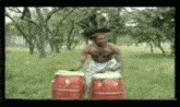 a man without a shirt is playing drums in a field with trees in the background