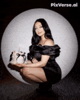 a woman in a black dress kneeling down holding a cake with a candle