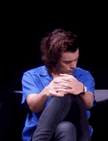 a young man with long hair is sitting with his legs crossed and his hands folded