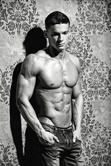 a shirtless man is standing in front of a wall with a floral pattern
