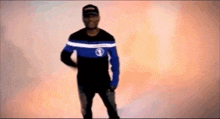 a man wearing a black and blue shirt and a hat is standing in front of a wall .