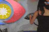 a woman in a black tank top stands in front of a colorful sign that says ' k-pop ' on the bottom