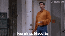 a man in an orange shirt is standing in front of a door holding a remote control and says morning biscuits