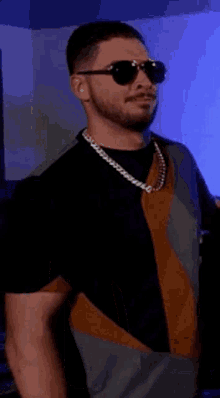 a man wearing sunglasses and a necklace is standing in front of a blue light .