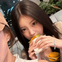 a girl eating a hamburger next to a picture of a hamburger on a bun