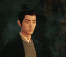 a man with a bun on his head is wearing a black jacket and a grey sweater
