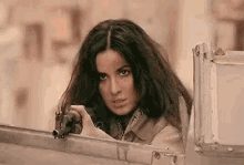 a woman is holding a gun in her hand and looking out a window .