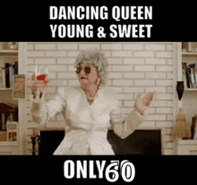 an older woman is holding a glass of wine in front of a fireplace with the words dancing queen young & sweet only 60 below her