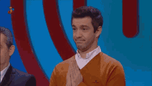 a man in an orange sweater is clapping in front of a blue background with the word sorpresa on it