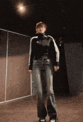 a woman in a black adidas jacket is standing in a dark room