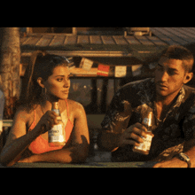 a man and a woman sit at a table drinking corona