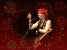 a man with red hair is singing into a microphone while fireworks are in the background