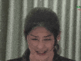 a close up of a woman 's face with a curtain behind her and a green x on the bottom right