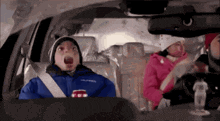 a boy in a columbia jacket is sitting in the back seat of a car with his mouth open