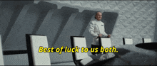 a man in a white suit stands in a conference room with the words best of luck to us both written in yellow