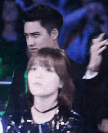 a man and a woman are sitting in a crowd and the woman is looking at the man